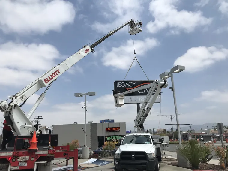 Crane lifting the Legacy Cars sign cabinet onto its pole