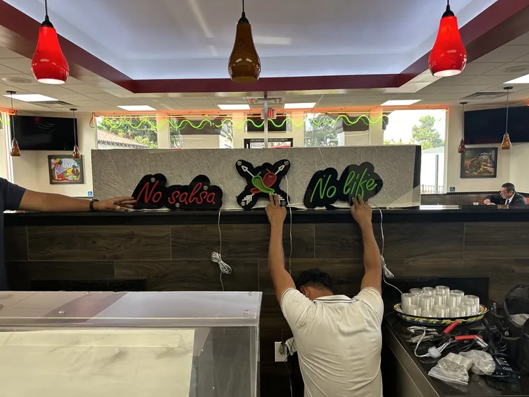 Installer hanging the No Salsa No Life neon signs in a restaurant