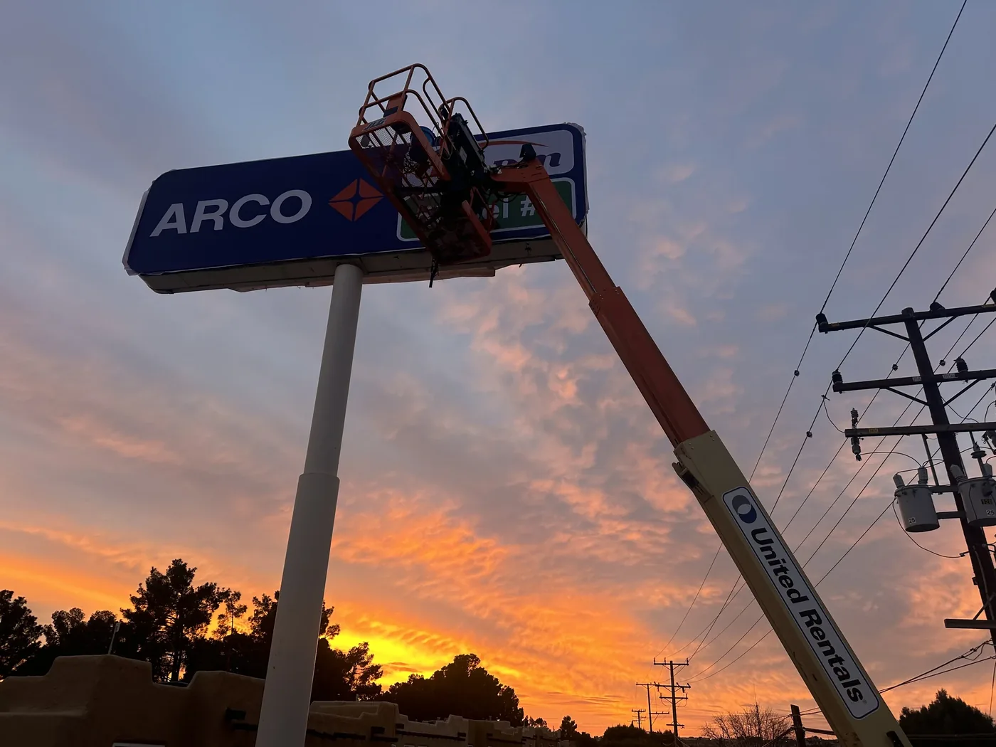 Boom lift at an ARCO pole sign at sunset
