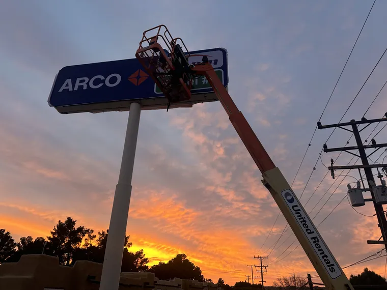Boom lift at an ARCO pole sign at sunset