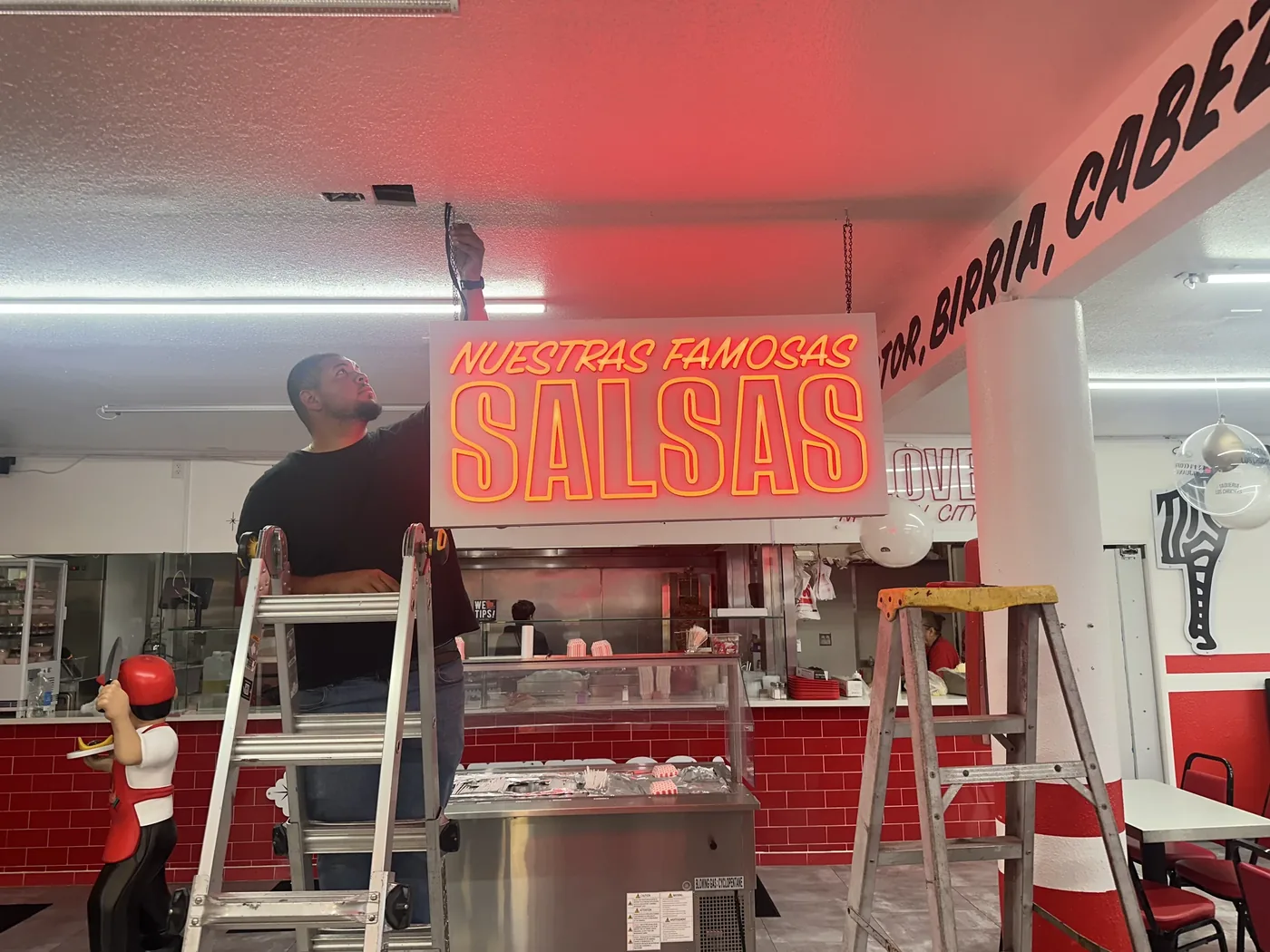 Installer hanging the Nuestras Famosas Salsas neon sign in a restaurant