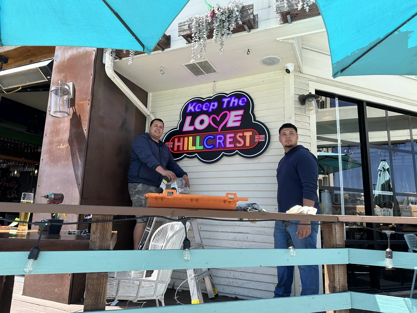Crew installing the Keep the Love Hillcrest neon sign on a patio wall