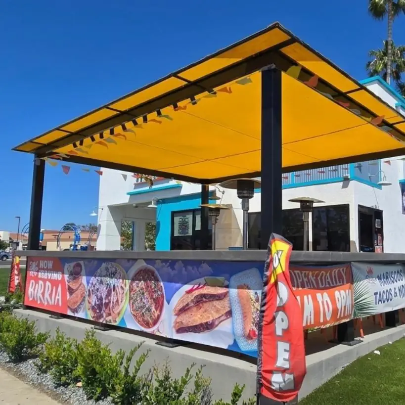 Yellow patio cover with printed birria menu banners at a taco shop
