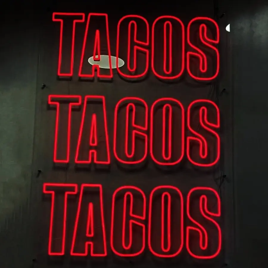 Red neon sign reading TACOS TACOS TACOS stacked on a dark wall