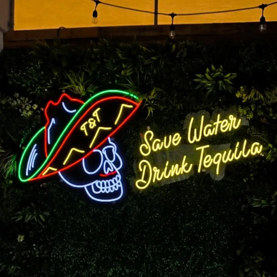 T and T taco skull neon sign reading Save Water Drink Tequila on a greenery wall