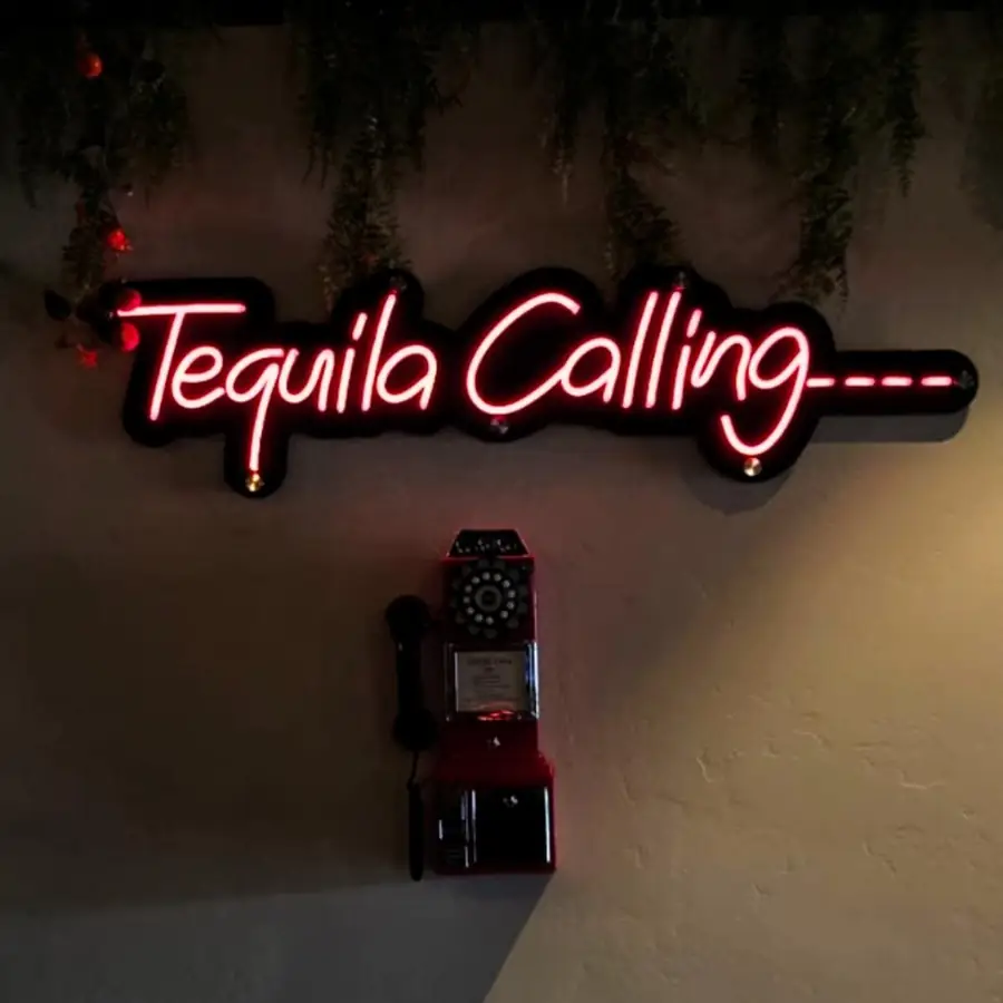 Tequila Calling neon sign above a vintage payphone