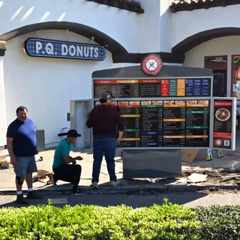 Crew setting a new outdoor menu board outside P.Q. Donuts