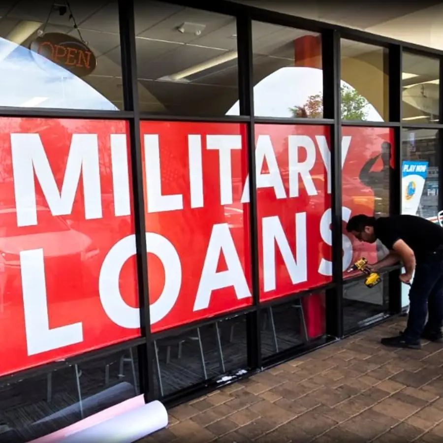 Installer applying red Military Loans window graphics to a storefront