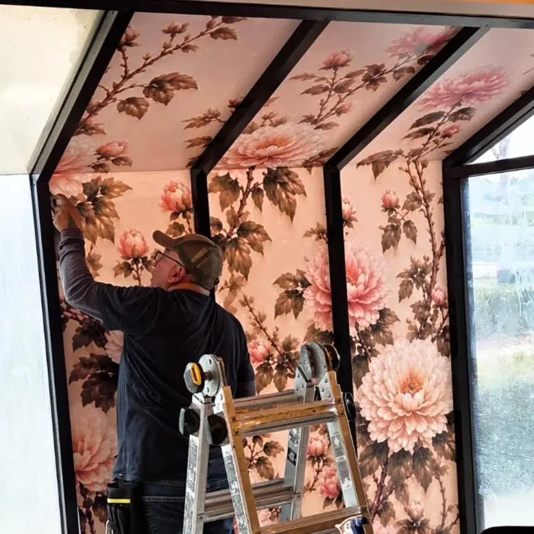 Installer fitting a floral wall mural around a window frame