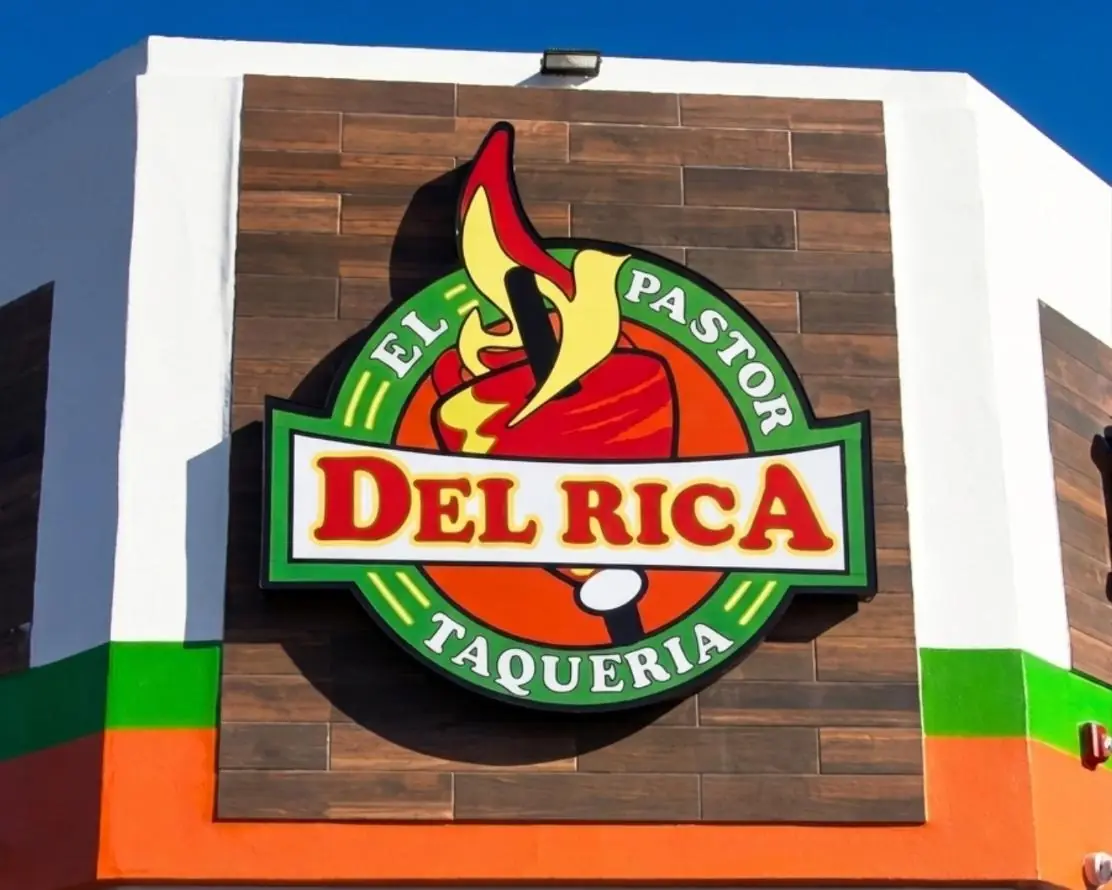 Del Rica Taqueria round logo sign mounted on a wood panel storefront