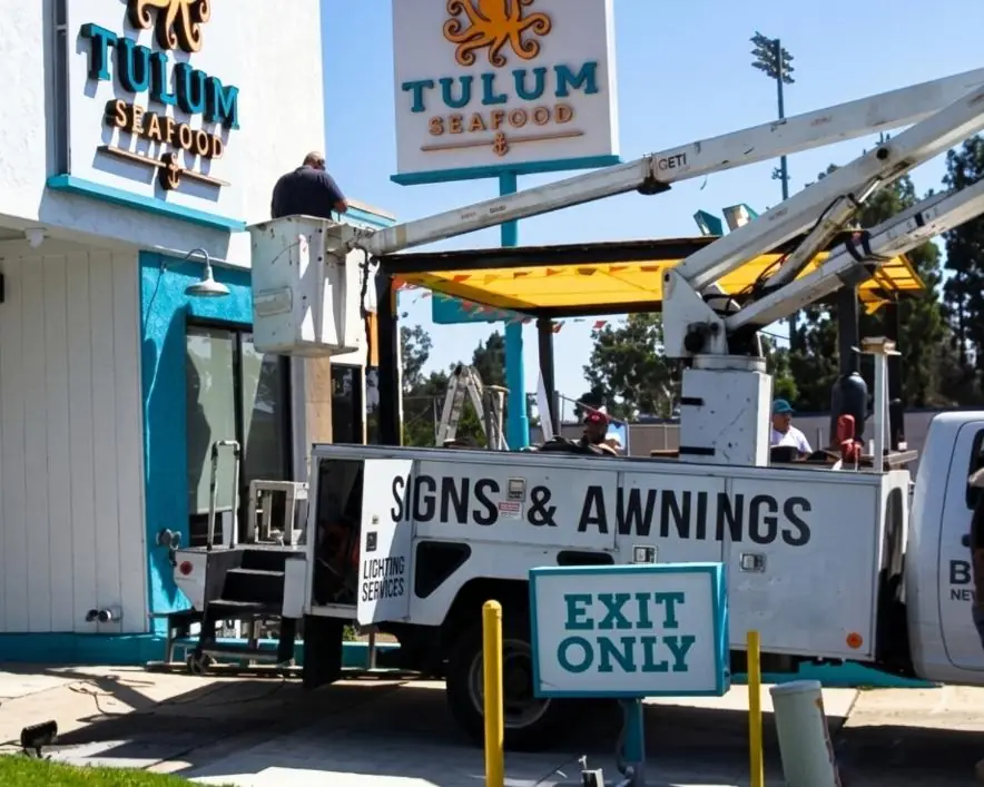 Best Deal bucket truck and crew installing signage and an awning at Tulum Seafood
