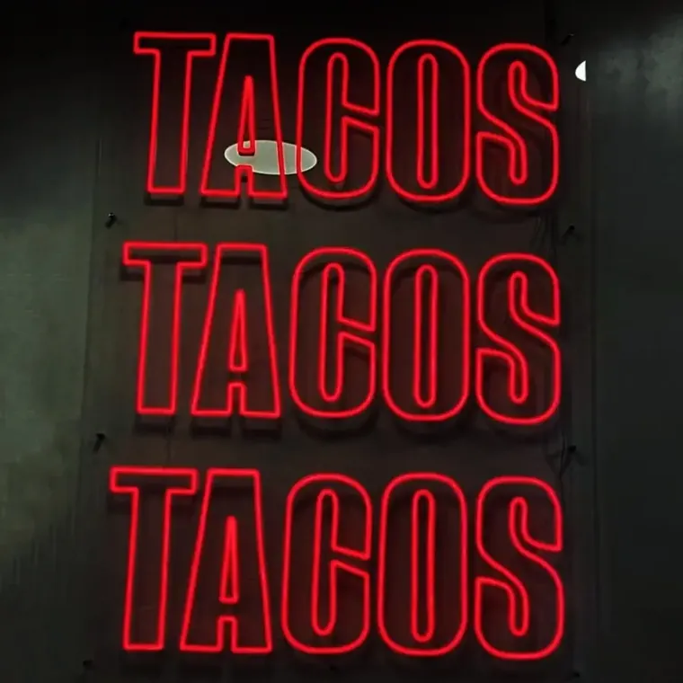 Red neon sign reading TACOS TACOS TACOS stacked on a dark wall