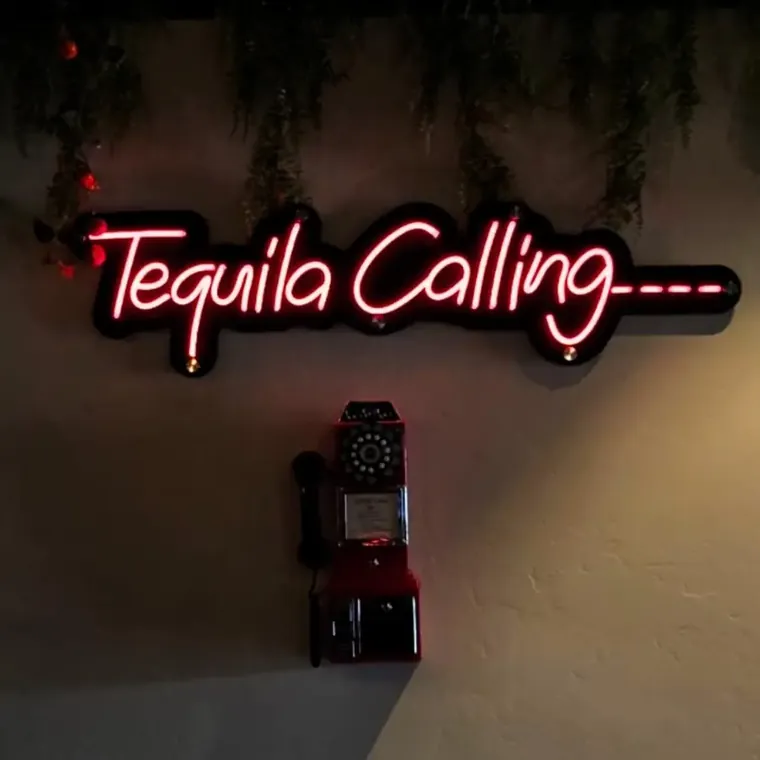 Tequila Calling neon sign above a vintage payphone